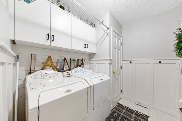 clothes washing area with cabinet space, independent washer and dryer, a decorative wall, a wainscoted wall, and a textured ceiling