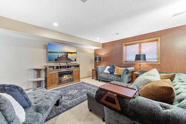 living room with carpet, a textured ceiling, baseboards, and a glass covered fireplace