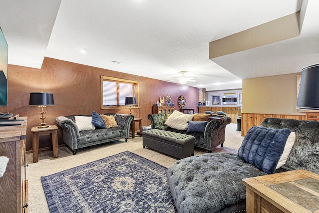 living area with carpet floors, ceiling fan, a wainscoted wall, and wood walls