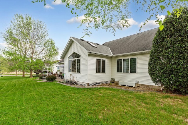back of property with a lawn, a shingled roof, and stairs