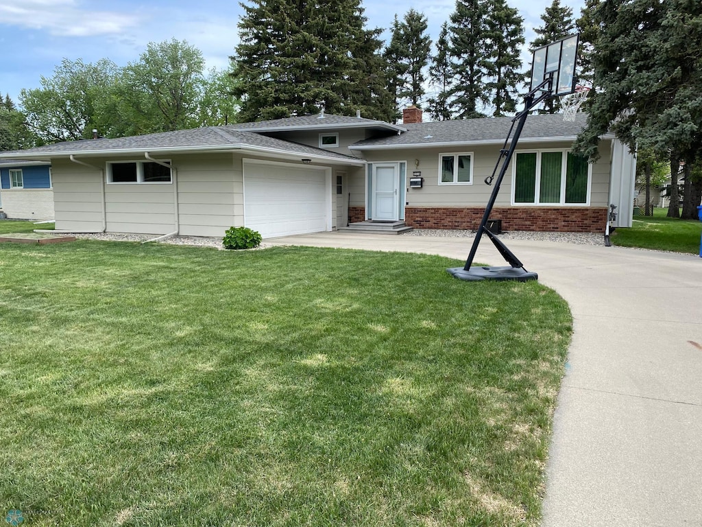 view of front of property with an attached garage, a front lawn, brick siding, and driveway