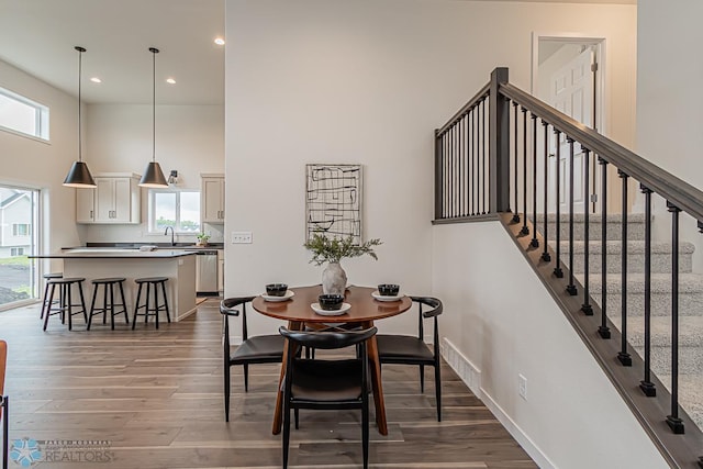dining area featuring a towering ceiling, healthy amount of natural light, wood finished floors, recessed lighting, and stairway