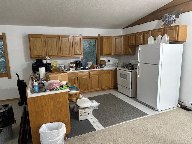 kitchen featuring white appliances, lofted ceiling, brown cabinets, light tile patterned floors, and a textured ceiling