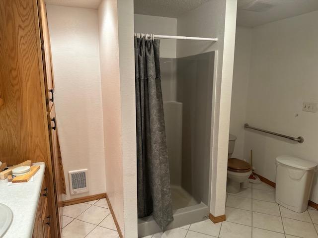 full bathroom featuring a stall shower, tile patterned floors, toilet, and vanity