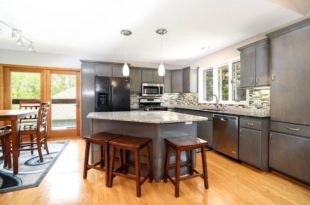 kitchen featuring appliances with stainless steel finishes, healthy amount of natural light, light wood-type flooring, and a kitchen bar