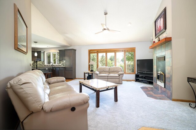 living area with a fireplace, a ceiling fan, plenty of natural light, light colored carpet, and high vaulted ceiling