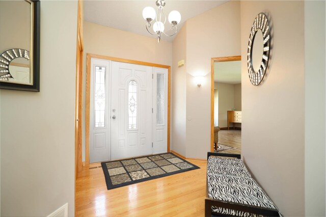 foyer entrance with wood finished floors, a chandelier, baseboards, and lofted ceiling