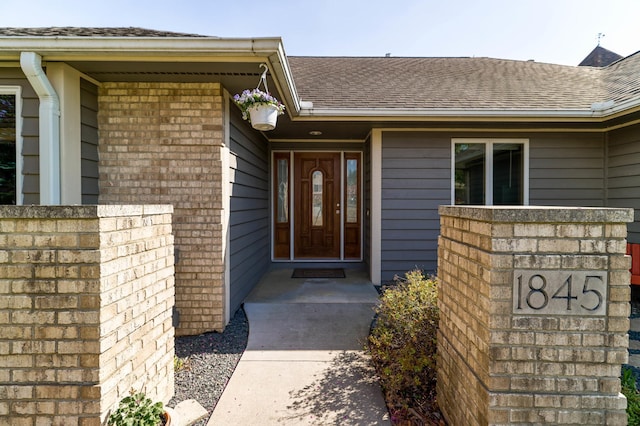 entrance to property with roof with shingles and brick siding