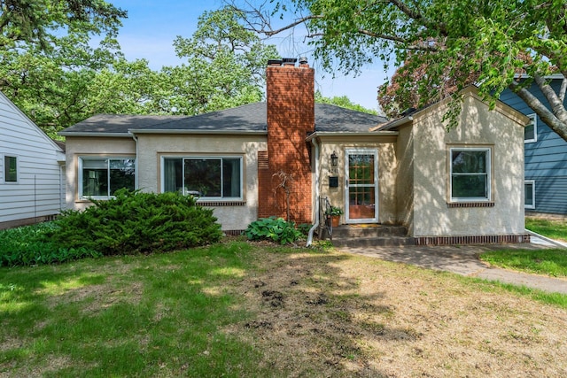 view of front of house with a front yard, a chimney, stucco siding, and a shingled roof