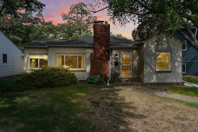 view of front of house with a chimney, a lawn, and stucco siding