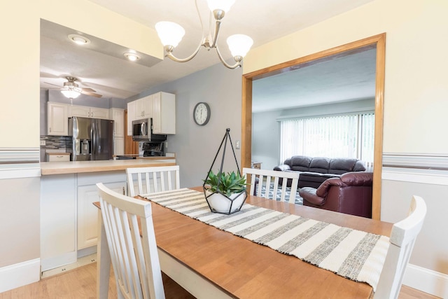 dining space featuring a chandelier, light wood finished floors, ceiling fan, and baseboards