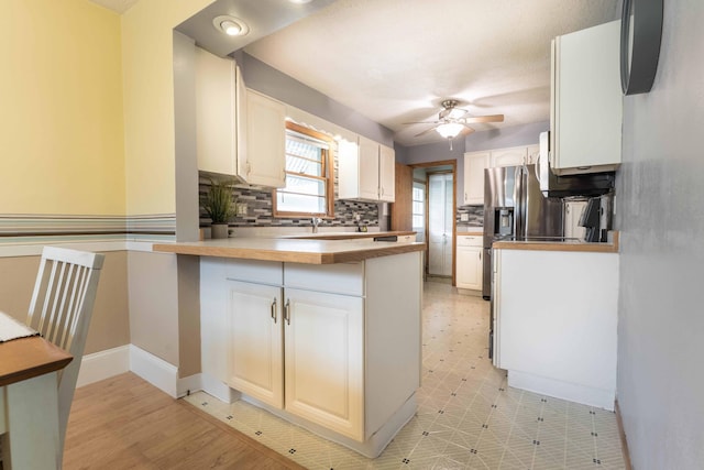 kitchen with a ceiling fan, a peninsula, backsplash, baseboards, and light flooring