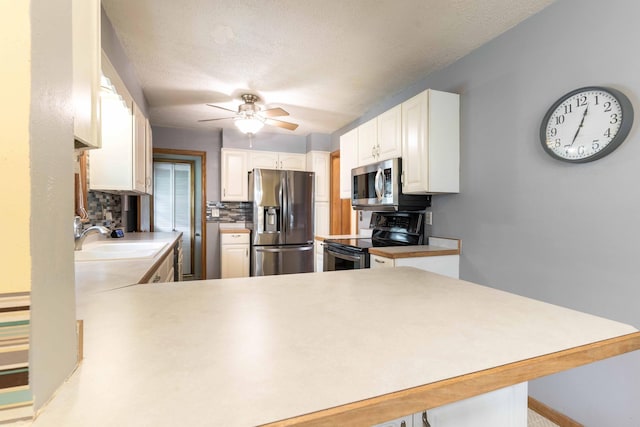 kitchen featuring appliances with stainless steel finishes, a sink, backsplash, ceiling fan, and a peninsula