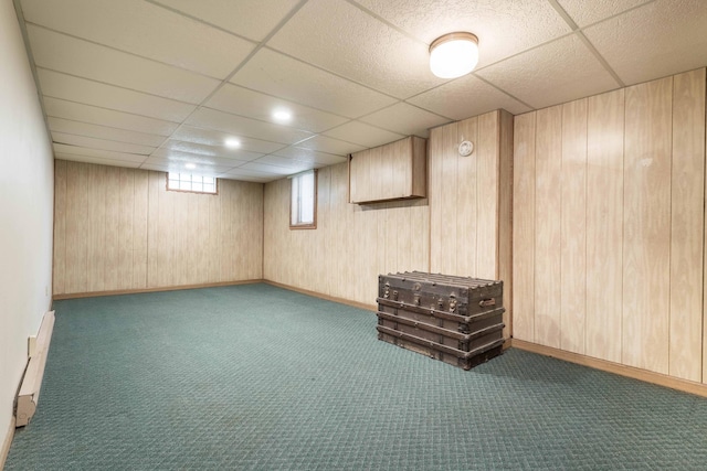 below grade area with carpet, a paneled ceiling, wood walls, and baseboards