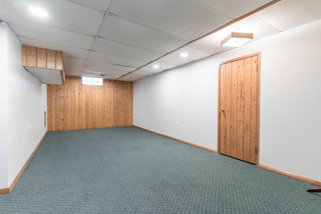 basement with carpet flooring, wood walls, a drop ceiling, recessed lighting, and baseboards