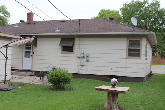 rear view of property featuring a chimney, a yard, a patio area, and a shingled roof