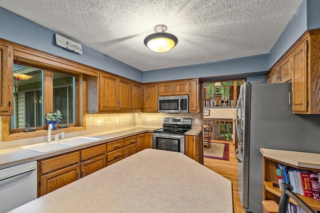480 Suzanne Ave, Shoreview, MN 55126 - kitchen with appliances with stainless steel finishes, a sink, light wood finished floors, brown cabinets, and a textured ceiling