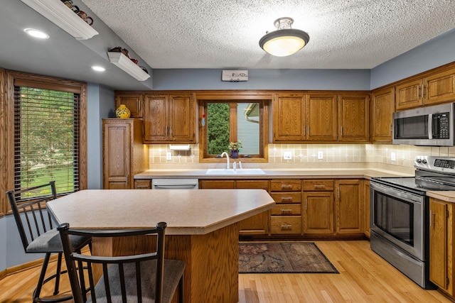 480 Suzanne Ave, Shoreview, MN 55126 - kitchen with stainless steel appliances, a sink, brown cabinets, light wood-type flooring, and a textured ceiling