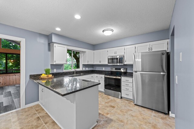 824 96th Ln NE, Blaine, MN 55434 - kitchen featuring stainless steel appliances, a peninsula, white cabinets, dark stone counters, and a textured ceiling