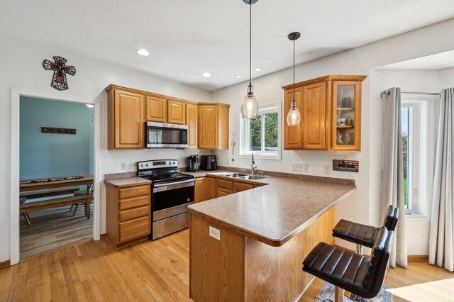 1005 Hope Ave, Jordan, MN 55352 - kitchen featuring appliances with stainless steel finishes, a sink, a peninsula, light wood-style floors, and a kitchen bar