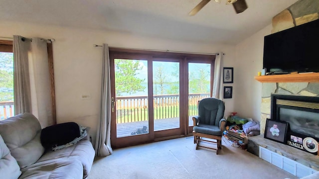living area with a ceiling fan, plenty of natural light, carpet, lofted ceiling, and a stone fireplace