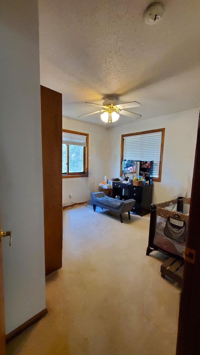 living area featuring carpet floors, a ceiling fan, a textured ceiling, and baseboards