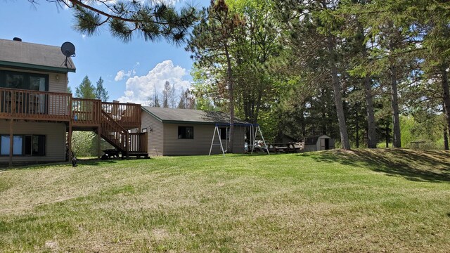 view of green lawn with stairway, a deck, a shed, and an outbuilding