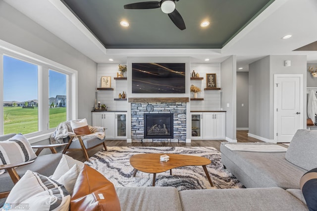 1991 69th Ave S, Fargo, ND 58104 - living room with a ceiling fan, wood finished floors, a tray ceiling, baseboards, and a stone fireplace