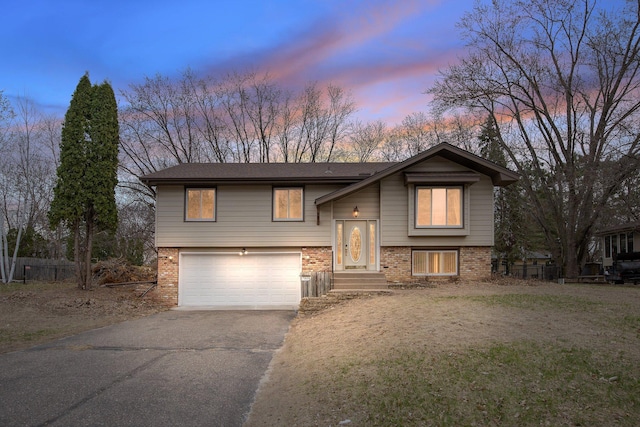 raised ranch with driveway, a garage, and brick siding