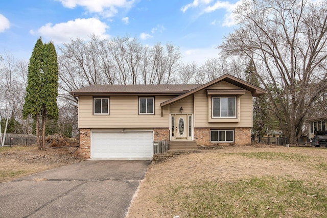bi-level home featuring brick siding, asphalt driveway, an attached garage, and fence