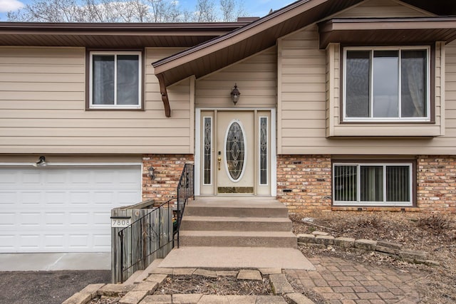 view of exterior entry with brick siding, a garage, and driveway
