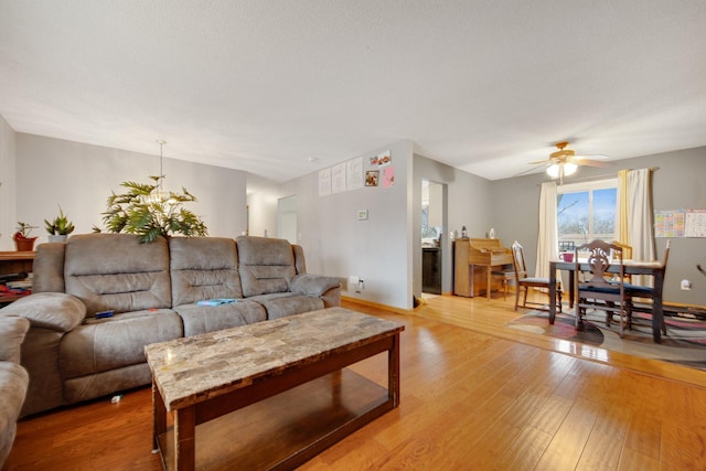 living area with light wood-type flooring, a ceiling fan, a chandelier, and baseboards