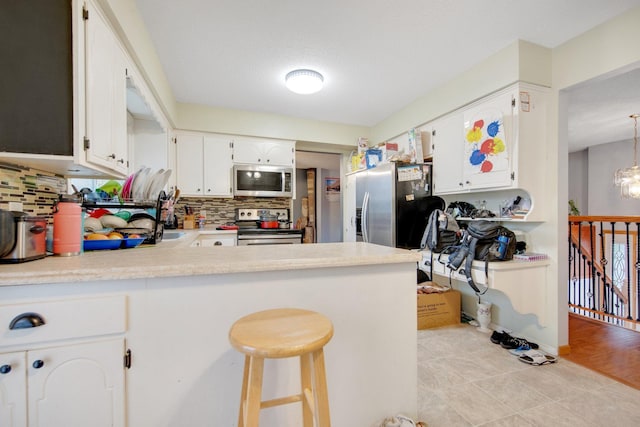 kitchen featuring stainless steel appliances, backsplash, a peninsula, light countertops, and white cabinets