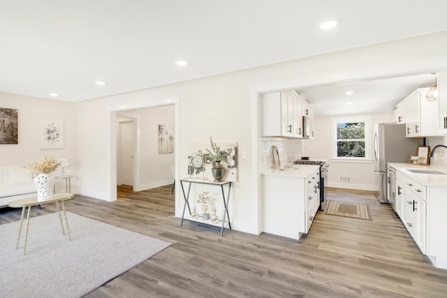 kitchen featuring stainless steel appliances, a sink, light countertops, light wood-style flooring, and tasteful backsplash