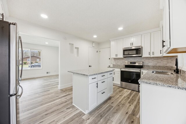 2581 Ardan Ave, Mounds View, MN 55112 - kitchen with appliances with stainless steel finishes, a sink, light wood-style floors, decorative backsplash, and a center island