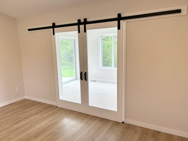 unfurnished room featuring a barn door, light wood finished floors, and baseboards