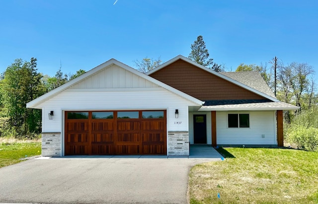 view of front of house featuring stone siding, a garage, roof with shingles, driveway, and a front lawn