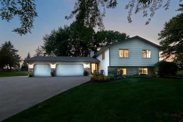 split level home with concrete driveway, a lawn, an attached garage, and a chimney