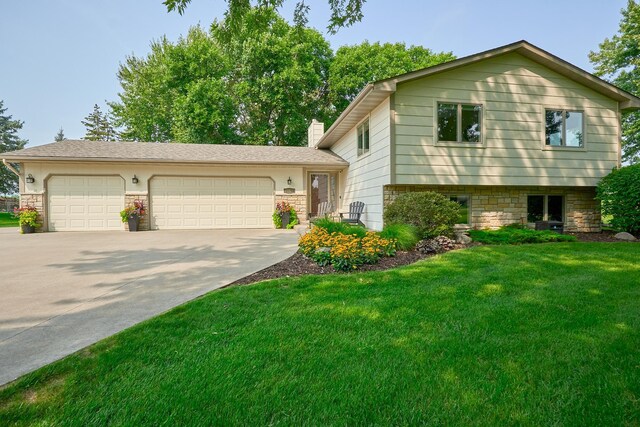 tri-level home featuring an attached garage, driveway, a front yard, and a chimney