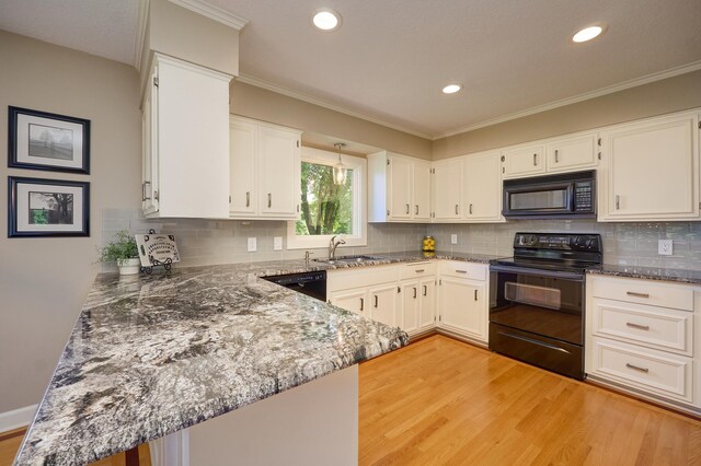 kitchen featuring black appliances, light wood finished floors, dark stone countertops, a sink, and recessed lighting