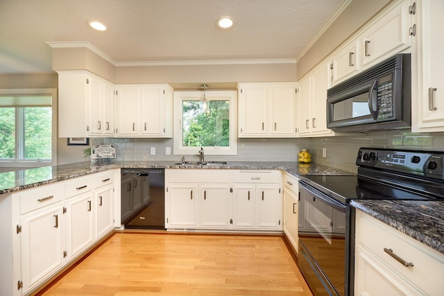 kitchen with black appliances, a sink, plenty of natural light, dark stone countertops, and crown molding