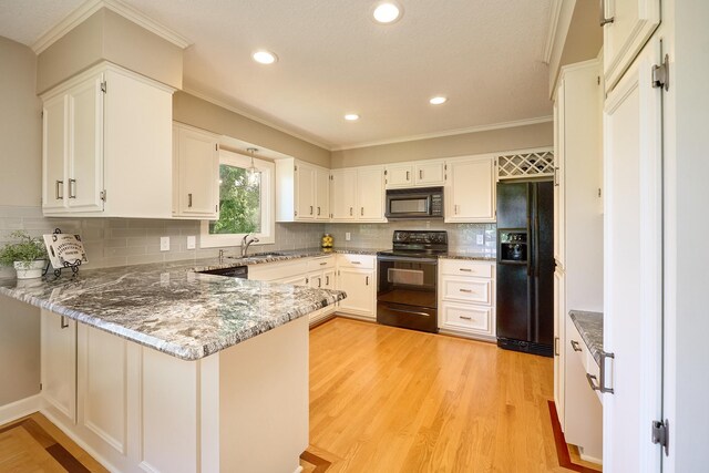 kitchen with black appliances, a peninsula, light stone counters, light wood-style flooring, and crown molding