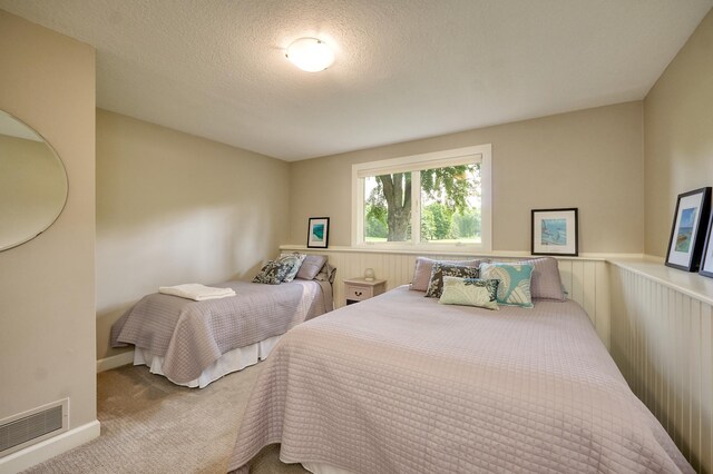 bedroom featuring carpet, a textured ceiling, and a wainscoted wall
