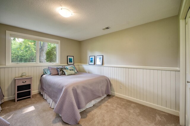 bedroom with carpet, a textured ceiling, wood walls, and a wainscoted wall