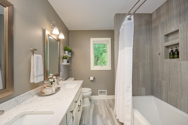 bathroom featuring toilet, shower / bath combo with shower curtain, double vanity, and baseboards