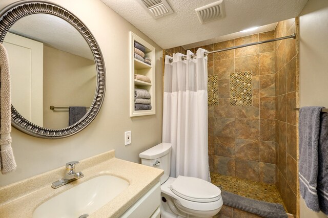 bathroom featuring tiled shower, toilet, vanity, and a textured ceiling