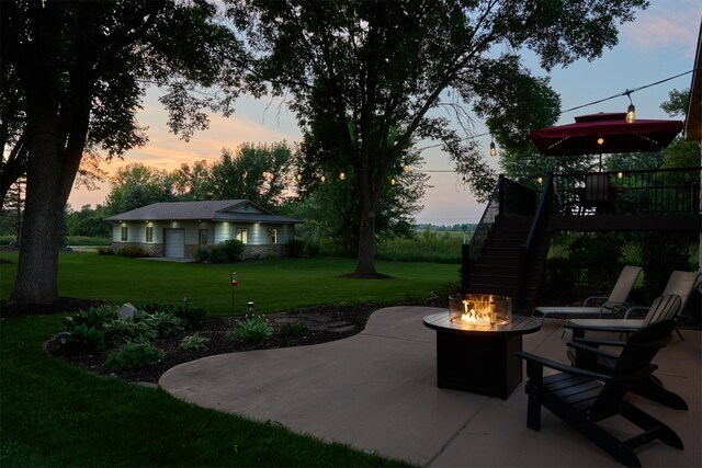 patio terrace at dusk featuring a fire pit, stairway, and a yard