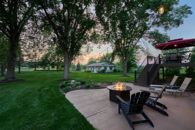 patio terrace at dusk featuring an outdoor fire pit, stairs, and a yard
