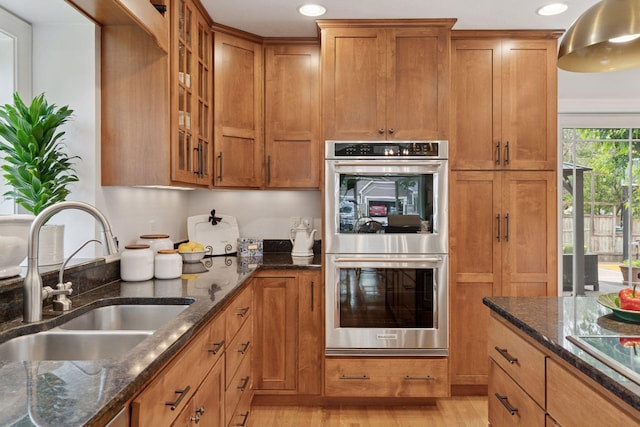 4084 Wild Goose Ln, White Bear Twp, MN 55110 - kitchen with stainless steel double oven, a sink, dark stone countertops, brown cabinetry, and glass insert cabinets