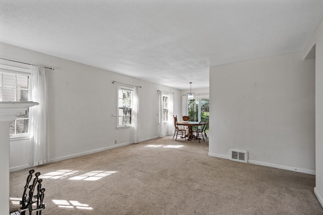 unfurnished living room featuring healthy amount of natural light, carpet flooring, a textured ceiling, and baseboards